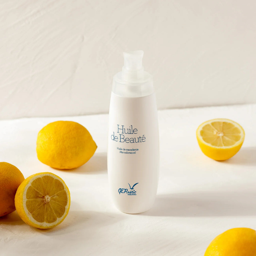 A white pump bottle labeled 'Huile de Beauté' with the brand name 'E-Relévé' at the bottom, styled on a white surface with whole and halved yellow lemons around it.