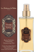 La Sultane de Saba 'Voyage sur la route des Epices' moisturizing mist, shown as a clear glass spray bottle filled with amber liquid next to its dark brown packaging box.