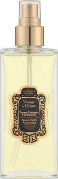 A clear rectangular spray bottle filled with pale yellow liquid, featuring a metallic gold pump and collar, and a decorative black label with gold ornamental border. The label reads 'Le Salon de Saffi' and 'Voyage d'Orient'.