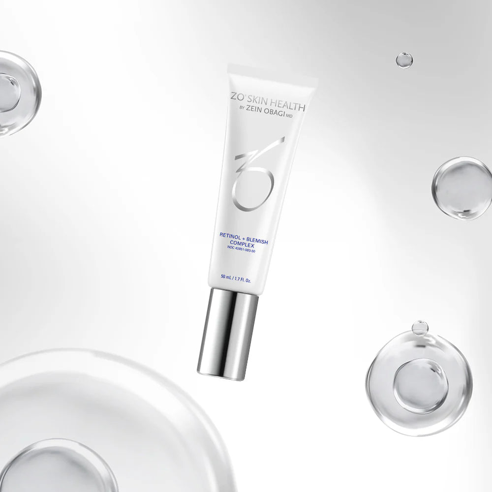 A white cosmetic tube labeled 'ZU SKIN HEALTH by ZEN ORAZO' with a metallic silver cap, floating diagonally on a clean white background with decorative clear liquid droplets and circular glass elements.
